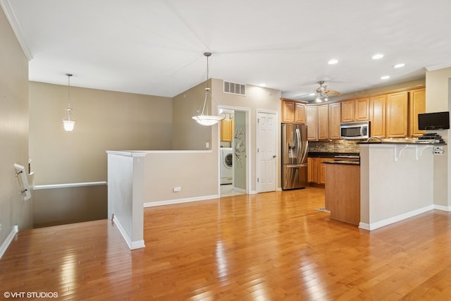 kitchen with light wood finished floors, a peninsula, appliances with stainless steel finishes, and washer / clothes dryer