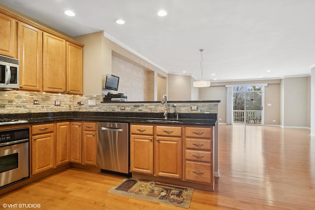 kitchen with appliances with stainless steel finishes, ornamental molding, a peninsula, light wood-style floors, and a sink