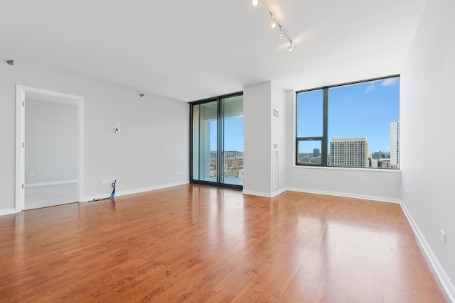 empty room featuring light wood finished floors, floor to ceiling windows, baseboards, and a city view