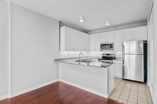 kitchen featuring a peninsula, appliances with stainless steel finishes, white cabinets, and a sink