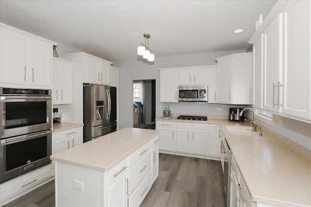 kitchen with stainless steel appliances, a sink, white cabinetry, light countertops, and dark wood-style floors