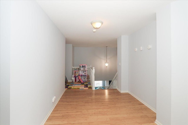 corridor with light wood-style floors, baseboards, and an upstairs landing