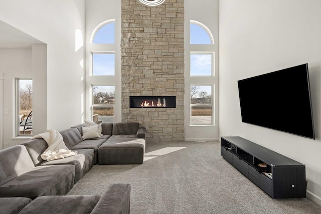 living area with light carpet, a towering ceiling, baseboards, and a stone fireplace