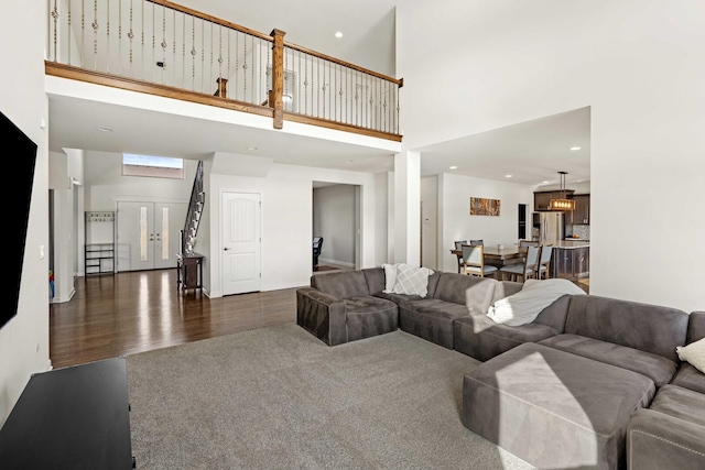 living area with dark wood-type flooring, recessed lighting, a towering ceiling, and dark colored carpet