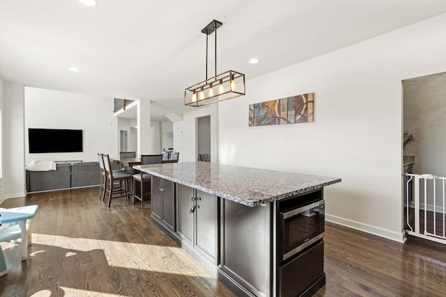 kitchen with a kitchen island, light stone counters, open floor plan, decorative light fixtures, and built in microwave