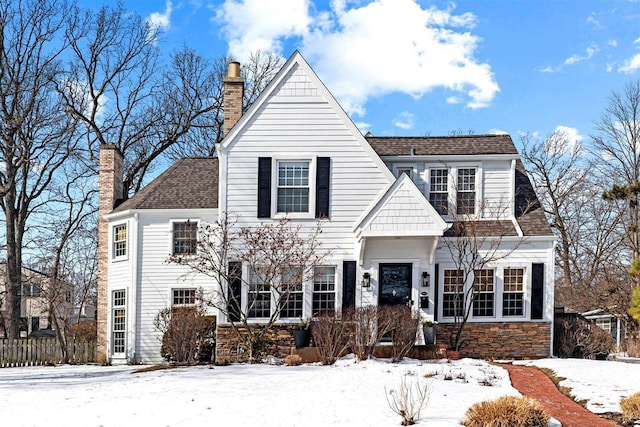 view of front of house featuring a shingled roof, stone siding, and a chimney