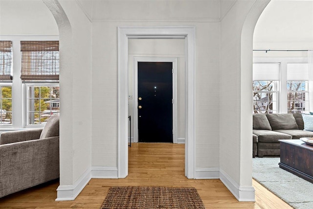 interior space featuring light wood-style floors, baseboards, and arched walkways