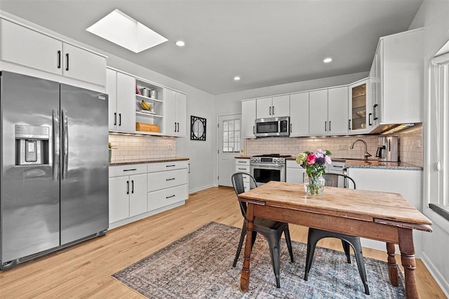 kitchen featuring appliances with stainless steel finishes, light wood-type flooring, white cabinets, and glass insert cabinets