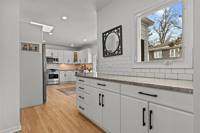 kitchen featuring light stone counters, stainless steel appliances, white cabinets, light wood finished floors, and glass insert cabinets