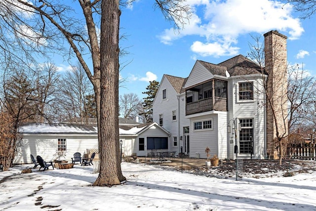 snow covered rear of property featuring a chimney and a balcony