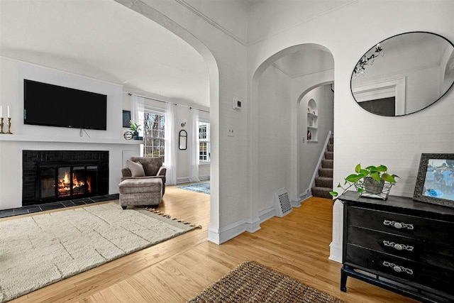 interior space featuring arched walkways, wood finished floors, stairway, and a glass covered fireplace