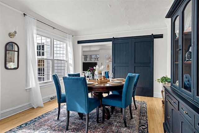 dining space with baseboards, a barn door, and light wood-style floors