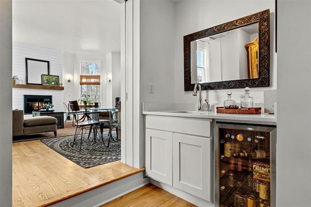 bar with light wood finished floors, beverage cooler, a sink, a fireplace, and indoor wet bar