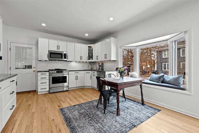 kitchen with decorative backsplash, dark countertops, glass insert cabinets, appliances with stainless steel finishes, and white cabinetry