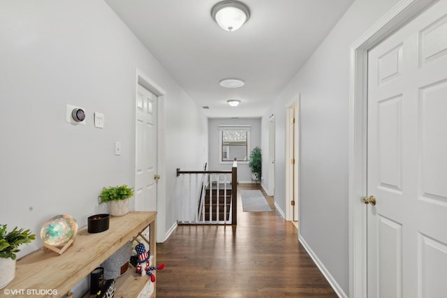 hall with dark wood-style flooring, an upstairs landing, and baseboards