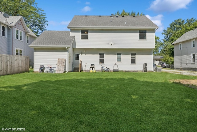 rear view of house featuring roof with shingles, a lawn, and fence