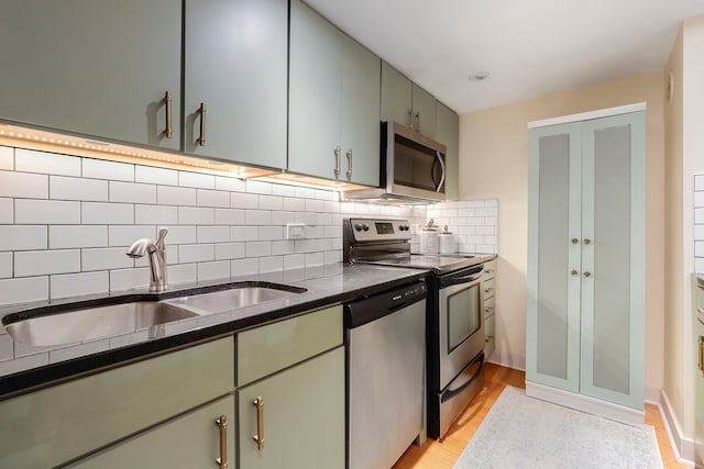 kitchen with stainless steel appliances, a sink, backsplash, light wood finished floors, and glass insert cabinets