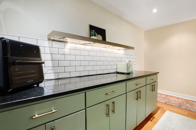 kitchen featuring dark countertops, green cabinetry, light wood finished floors, and decorative backsplash