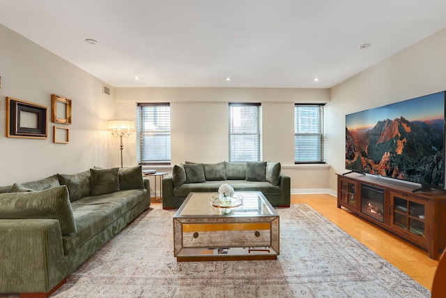 living area featuring light wood-type flooring, visible vents, plenty of natural light, and baseboards