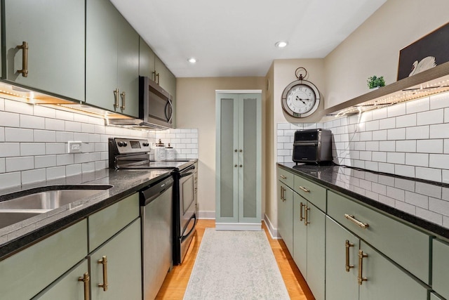 kitchen with stainless steel appliances, green cabinetry, and backsplash