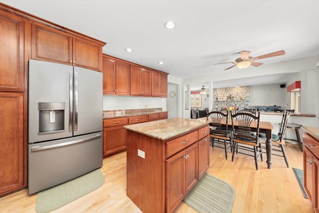 kitchen featuring light stone counters, a kitchen island, light wood-type flooring, stainless steel refrigerator with ice dispenser, and brown cabinets