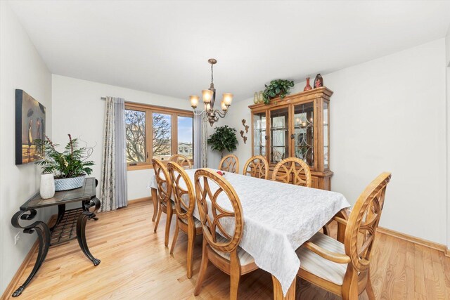 dining area with baseboards, light wood-style flooring, and an inviting chandelier