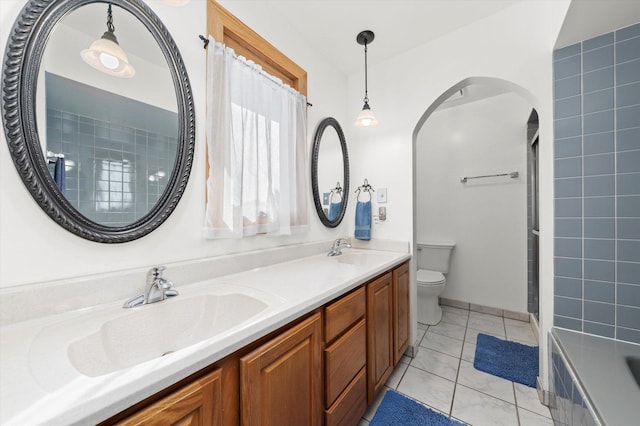 bathroom featuring a sink, a tile shower, toilet, and double vanity