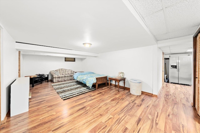 bedroom featuring baseboards, a paneled ceiling, light wood-style flooring, and stainless steel fridge with ice dispenser