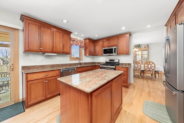 kitchen with stainless steel appliances, brown cabinetry, light wood-type flooring, and light stone countertops