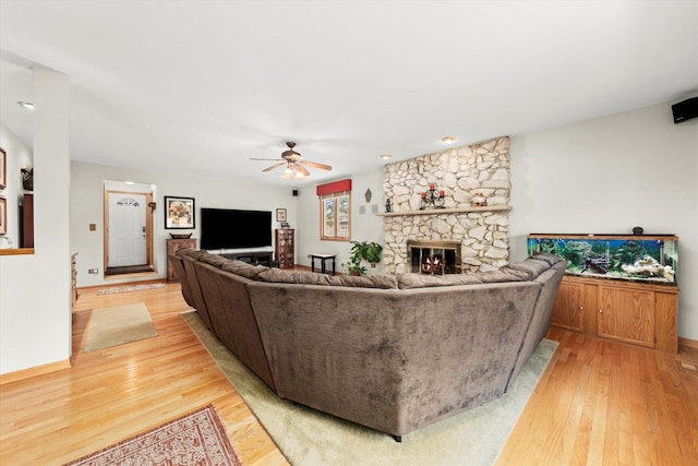 living area with ceiling fan, a stone fireplace, and light wood-style flooring