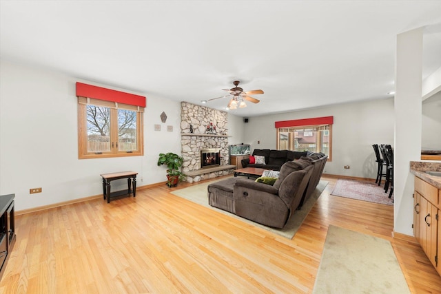 living room with light wood finished floors, a stone fireplace, and a wealth of natural light