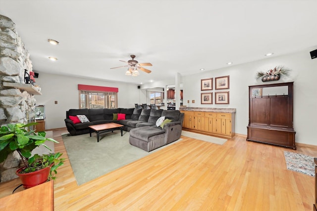 living room featuring light wood finished floors, recessed lighting, ceiling fan, a stone fireplace, and baseboards