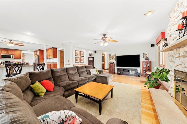 living room featuring light wood finished floors, a fireplace, and a ceiling fan