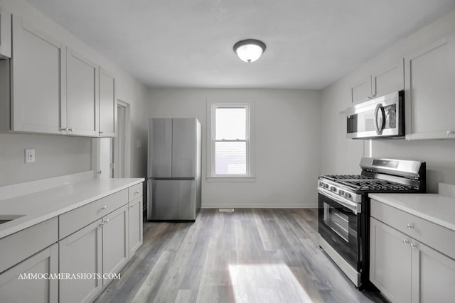 kitchen with appliances with stainless steel finishes, light countertops, light wood-style floors, and baseboards