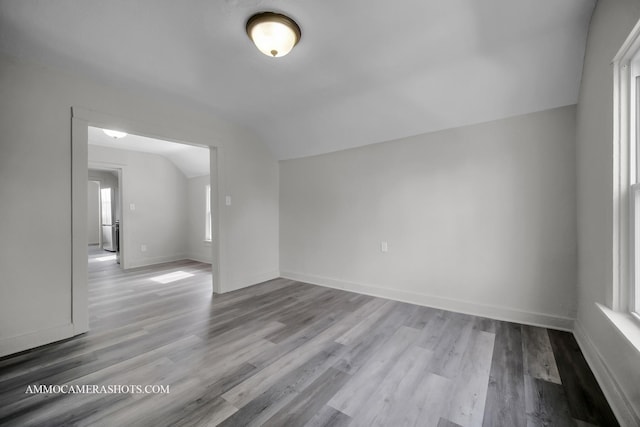 empty room featuring lofted ceiling, light wood finished floors, and baseboards