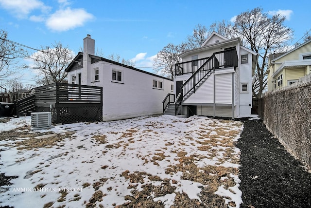 snow covered back of property with a chimney, central air condition unit, stairway, fence, and a deck