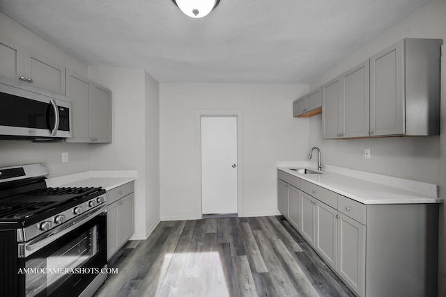 kitchen featuring stainless steel appliances, gray cabinets, light countertops, a sink, and light wood-type flooring