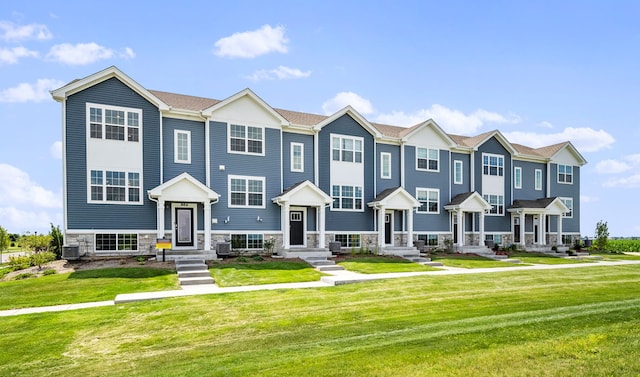 townhome / multi-family property featuring central air condition unit, stone siding, a residential view, and a front yard