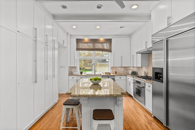 714 Sheridan Rd, Evanston, IL 60202 - kitchen with stainless steel appliances, a sink, light wood-style floors, backsplash, and white cabinetry