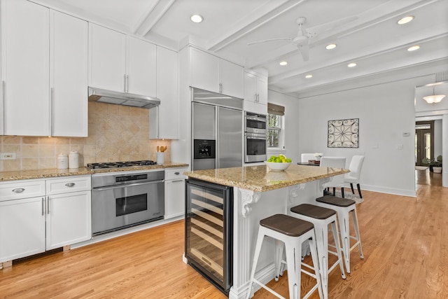 714 Sheridan Rd, Evanston, IL 60202 - kitchen featuring beverage cooler, under cabinet range hood, stainless steel appliances, a kitchen bar, and beamed ceiling