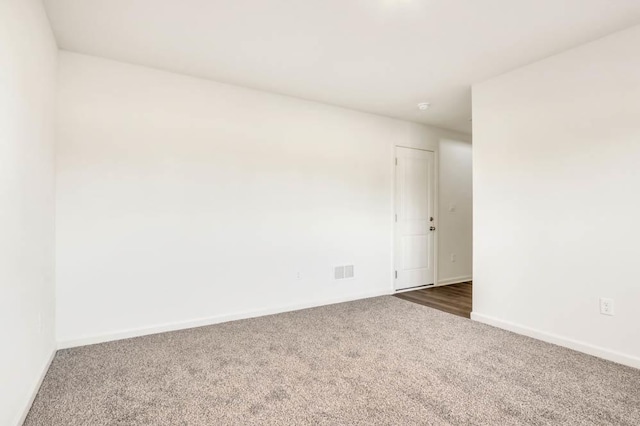 spare room with dark carpet, visible vents, and baseboards