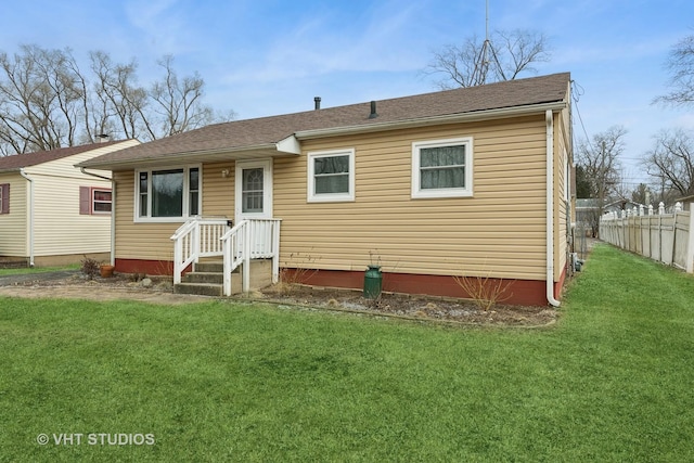 rear view of house featuring roof with shingles, fence, and a yard