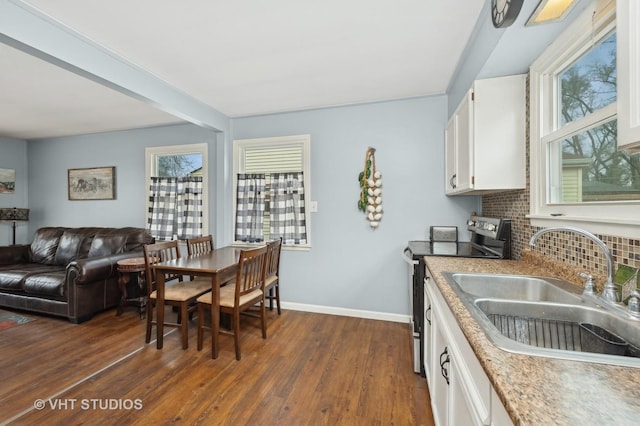 kitchen with open floor plan, a sink, stainless steel range with electric stovetop, white cabinetry, and backsplash