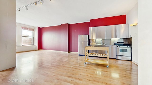 kitchen with appliances with stainless steel finishes, track lighting, a sink, and light wood-type flooring