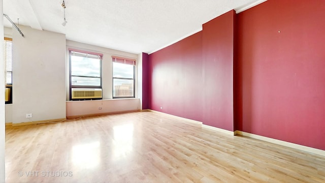 spare room with baseboards, cooling unit, and wood finished floors