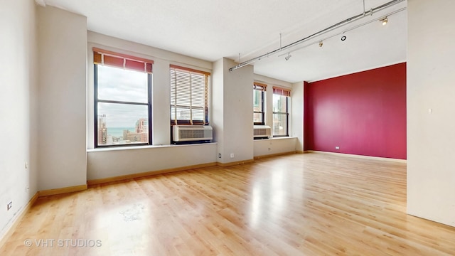 spare room with baseboards, rail lighting, wood finished floors, and cooling unit