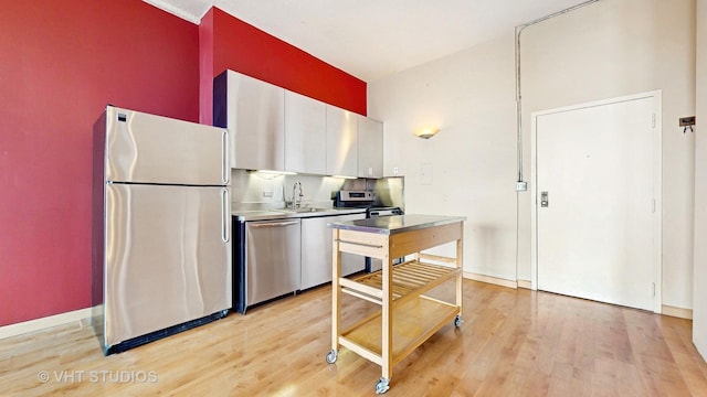 kitchen with appliances with stainless steel finishes, stainless steel counters, light wood-type flooring, a sink, and white cabinets