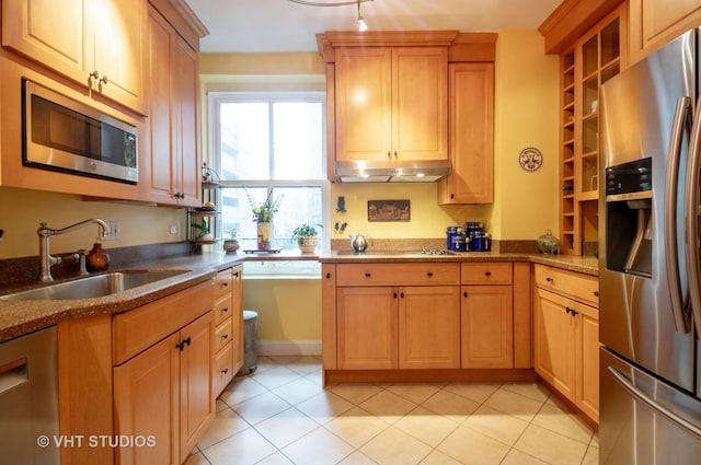 kitchen featuring light tile patterned floors, under cabinet range hood, a sink, appliances with stainless steel finishes, and dark stone countertops