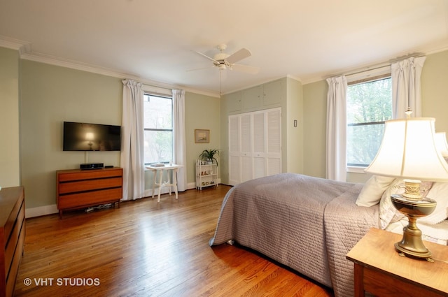 bedroom with baseboards, a ceiling fan, wood finished floors, crown molding, and a closet