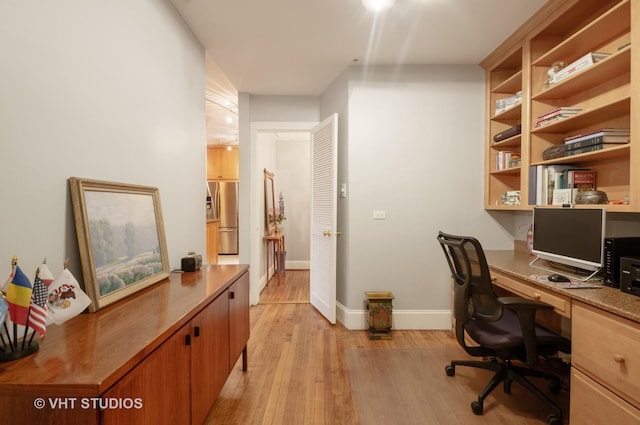 office area with baseboards, built in desk, and light wood finished floors